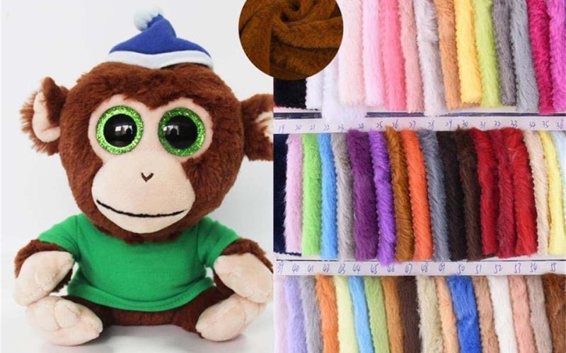 Plush monkey toy made with soft plush fabric alongside a wide color swatch chart of plush toy fabrics, showing pile texture, thickness, and color options commonly used in stuffed animal manufacturing