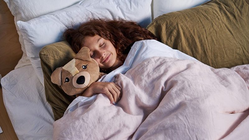 Girl sleeping peacefully while cuddling a weighted stuffed animal under a blanket