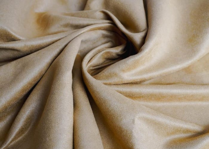 Close-up of beige faux suede fabric with soft, smooth texture, folded in gentle swirls to show drape and surface finish