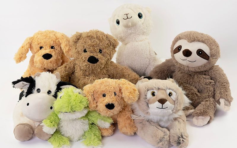 Assorted plush animals arranged in a group on a white background, including dogs, a sloth, a zebra, and other soft stuffed toys