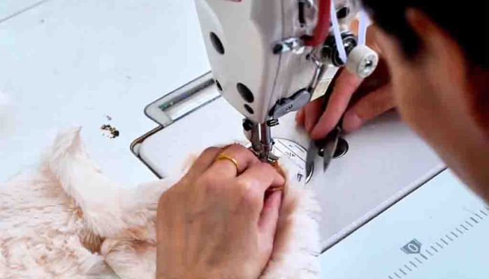 Close-up of hands using a sewing machine to stitch soft plush fabric for toy making.