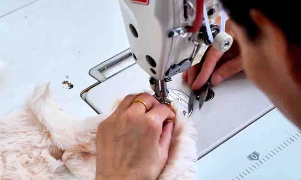 Close-up of hands using a sewing machine to stitch soft plush fabric for toy making.