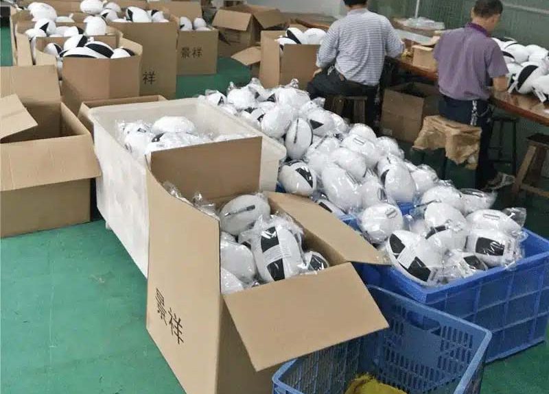 Workers packing finished plush toys into cartons and plastic bags in a factory setting, preparing bulk orders for shipment.