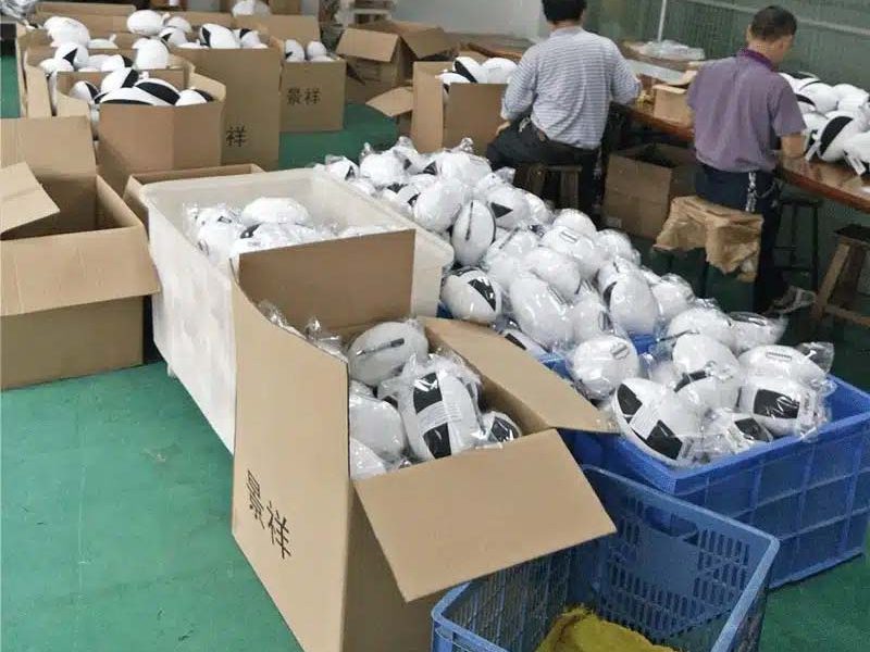 Workers packing finished plush toys into cartons and plastic bags in a factory setting, preparing bulk orders for shipment.