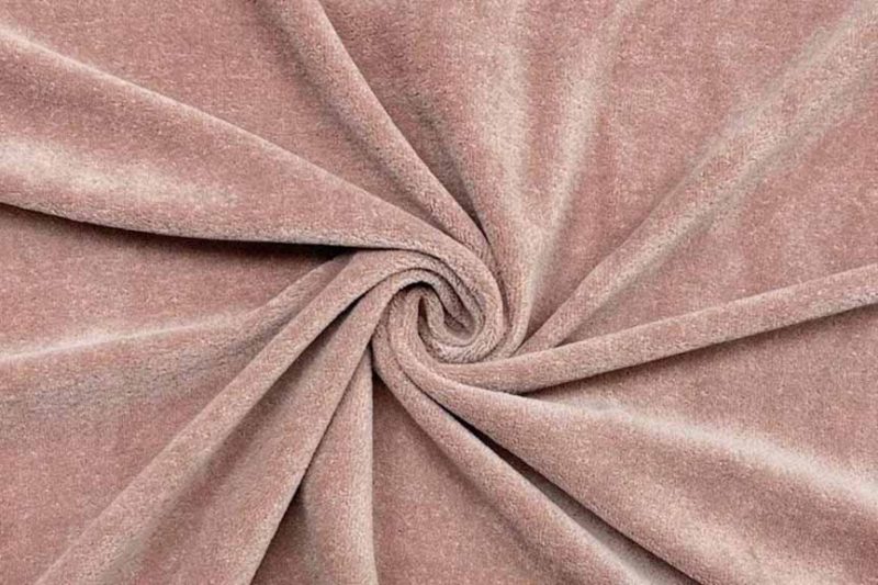 Close-up of soft blush-toned velour fabric arranged in a spiral fold, highlighting short pile texture, gentle sheen, and smooth hand feel commonly used in plush toy surfaces.