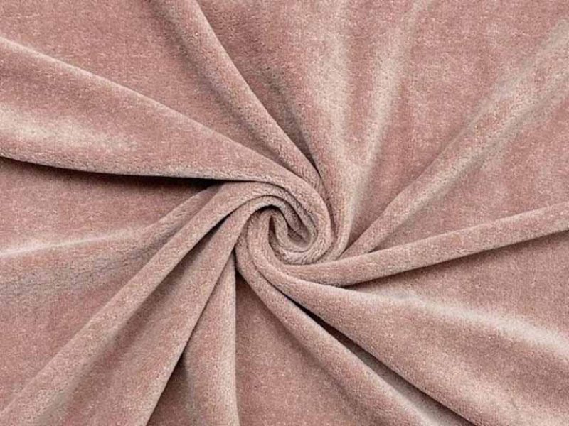 Close-up of soft blush-toned velour fabric arranged in a spiral fold, highlighting short pile texture, gentle sheen, and smooth hand feel commonly used in plush toy surfaces.