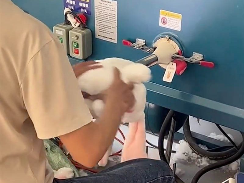 A factory worker fills a plush toy with stuffing using industrial equipment during the production process. The image highlights an important manufacturing stage where the toy’s softness, shape, and fullness are formed before final closing and quality inspection.