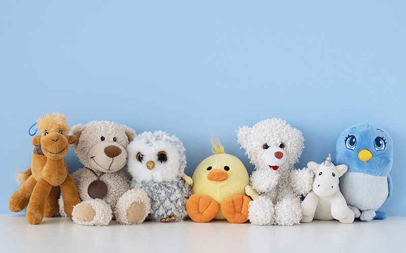 Two children sitting on a bed surrounded by colorful plush toys, showing how stuffed animals provide comfort, fun, and companionship during playtime.