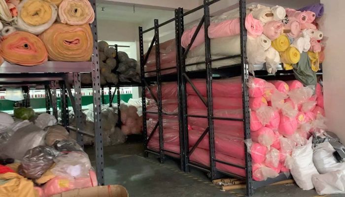 Shelves filled with colorful rolls of plush fabric stored in a warehouse for toy manufacturing.