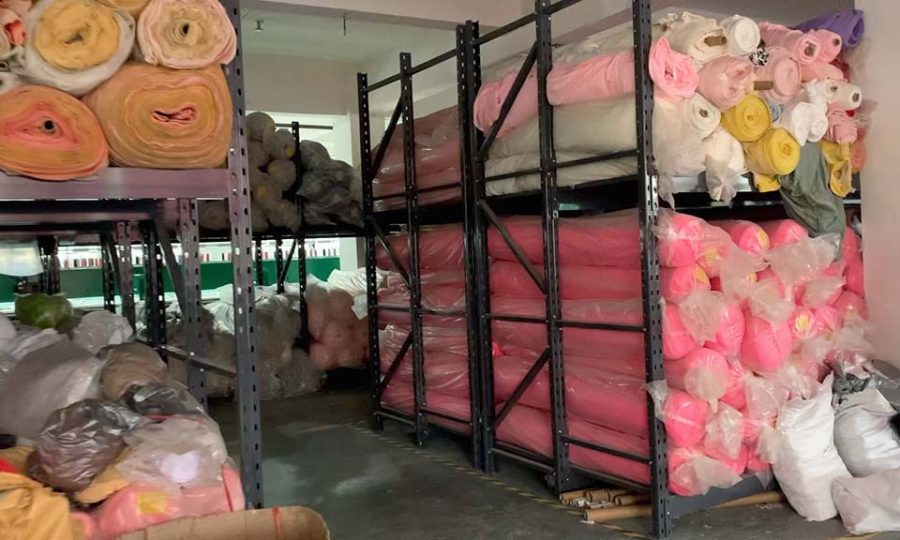 Shelves filled with colorful rolls of plush fabric stored in a warehouse for toy manufacturing.
