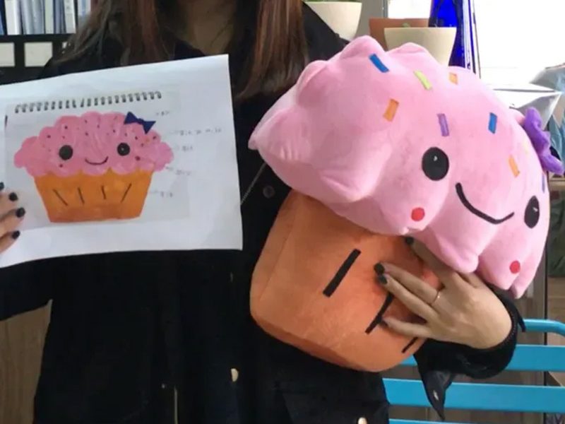 A custom plush toy developed from an original design drawing, showcasing the transformation from concept to finished product.