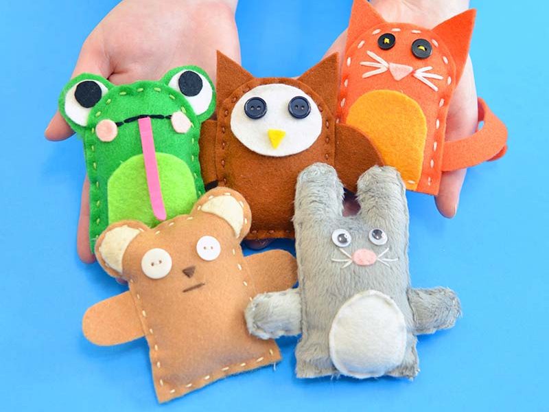 Hand holding five small handmade felt finger puppets shaped like animals on a blue background