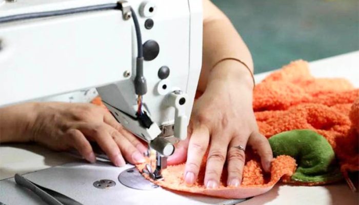 Worker using an industrial sewing machine to stitch orange plush fabric during stuffed toy manufacturing, showing precise stitching and professional production quality.