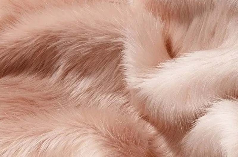 A close-up view of luxurious pink faux fur fabric with long, silky fibers and a smooth, lustrous texture, ideal for plush toys and home textiles.
