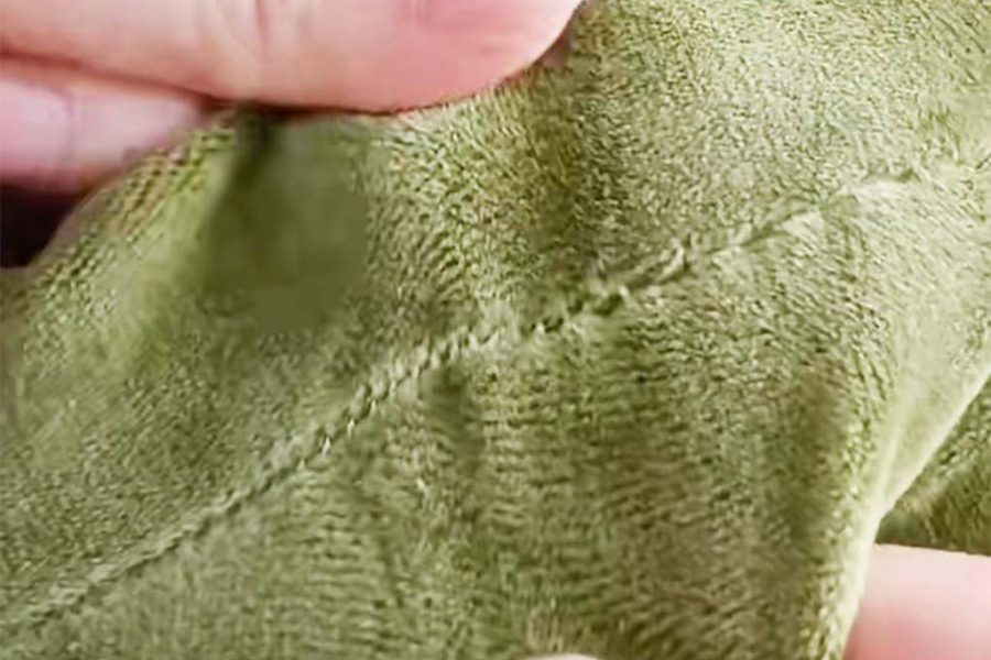 Close-up of hands holding green plush fabric showing a neatly sewn hidden stitch, demonstrating professional sewing technique used in plush toy manufacturing.