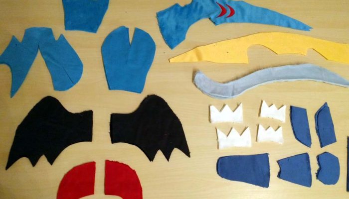 Various cut fabric pattern pieces laid out for assembling a custom plush toy, including wings, body panels, tail shapes, and decorative elements.
