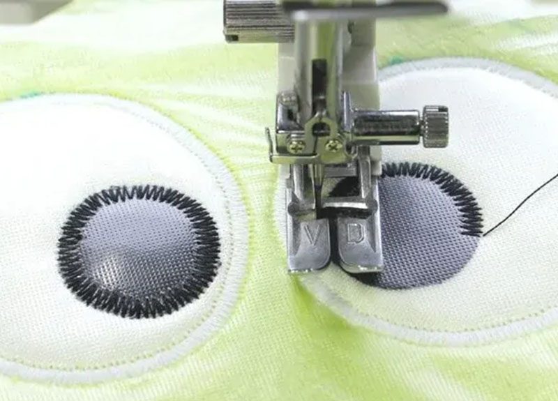 Close-up view of a sewing machine embroidering cartoon eyes onto soft plush fabric, showcasing precision stitching for plush toy detailing.