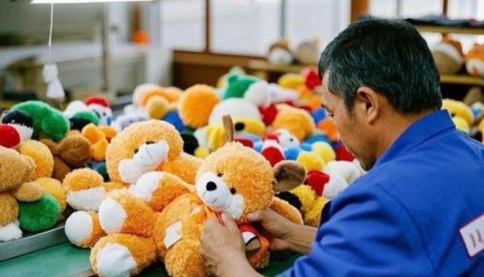Factory worker checking a teddy bear among colorful plush toys during quality inspection at a plush toy manufacturing workshop.
