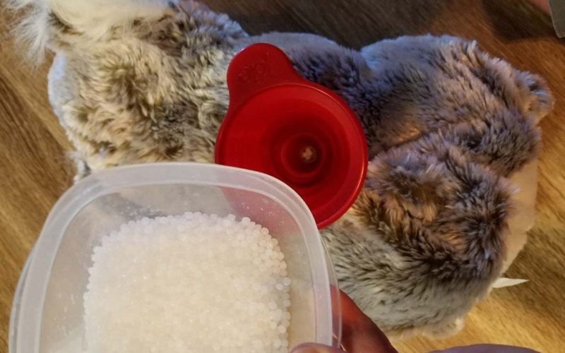 Close-up of poly-pellet beads being poured through a red funnel into a plush toy to add weight.