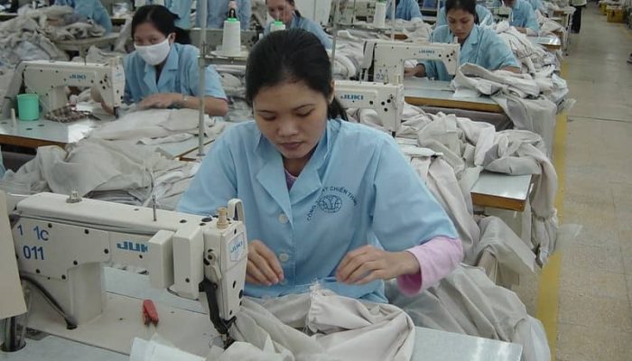 Workers in a garment factory using industrial sewing machines to stitch fabric pieces.