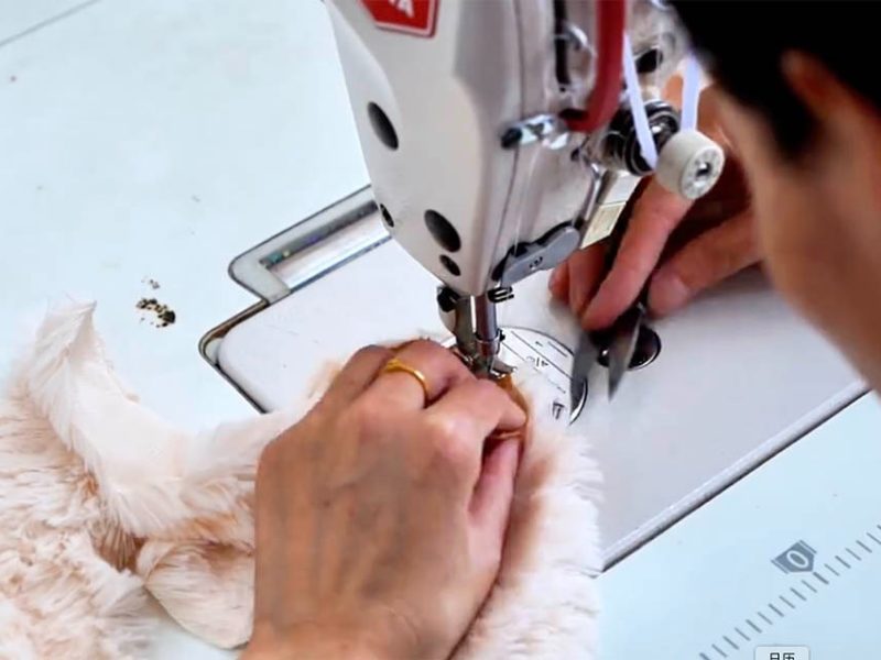 Hands sewing soft plush fabric with an industrial sewing machine during stuffed toy production.
