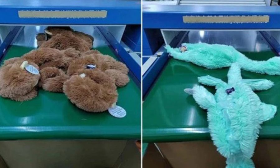 Plush toys lying flat on a green conveyor belt as they pass through an industrial needle-detection machine during factory safety inspection.