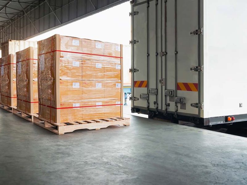 Stacks of cardboard boxes wrapped in plastic and secured on wooden pallets, ready to be loaded into a truck for delivery.