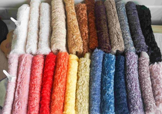Multiple rolls of soft plush fabric in various colors including pink, brown, blue, yellow, and purple, neatly arranged for stuffed toy production.