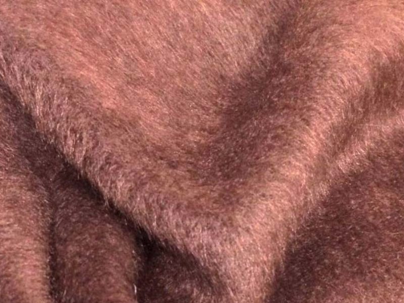 Close-up view of soft short-pile brown plush fabric showing its smooth texture and dense fibers, commonly used in plush toys and teddy bear manufacturing.