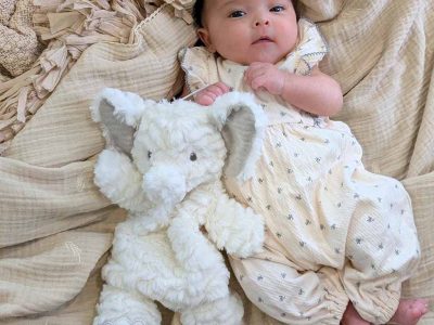 Infant lying on soft blankets while holding a fluffy white elephant stuffed toy.