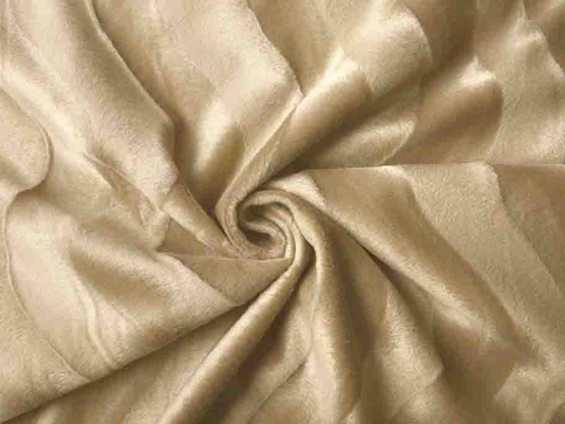 Close-up of soft light beige velboa fabric with a smooth short pile texture, arranged in a swirl pattern.