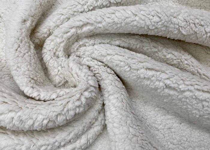 Close-up view of white sherpa plush fabric showing its fluffy, textured surface and natural folds.
