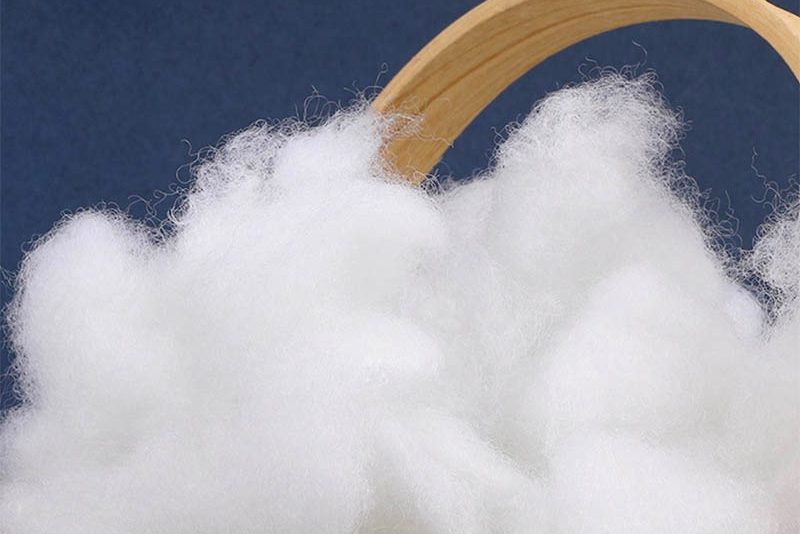 Fluffy white polyester fiberfill used as plush toy stuffing, displayed in a wooden container to show its softness, bounce, and high-loft quality.