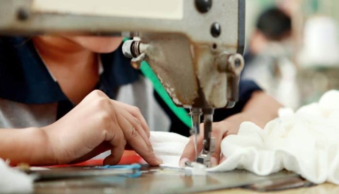 Close-up of a worker using an industrial sewing machine to stitch white fabric, showing hands guiding the material during plush toy production.