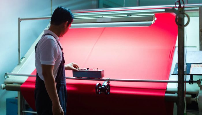 Technician inspecting bright red fabric on a textile production line under controlled lighting to ensure quality and consistency.
