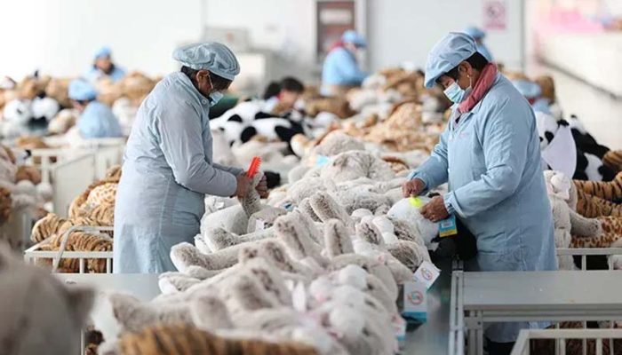 Workers in protective uniforms inspecting and grooming plush toys inside a large stuffed-animal manufacturing factory.
