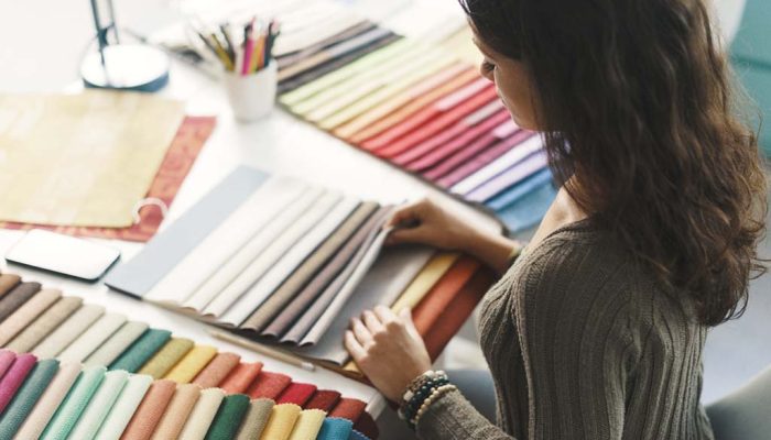 A woman examining a variety of colorful fabric swatches laid out on a desk, selecting materials for design work.